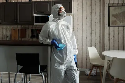 Worker in a white protective suit, respirator and goggles in a home kitchen
